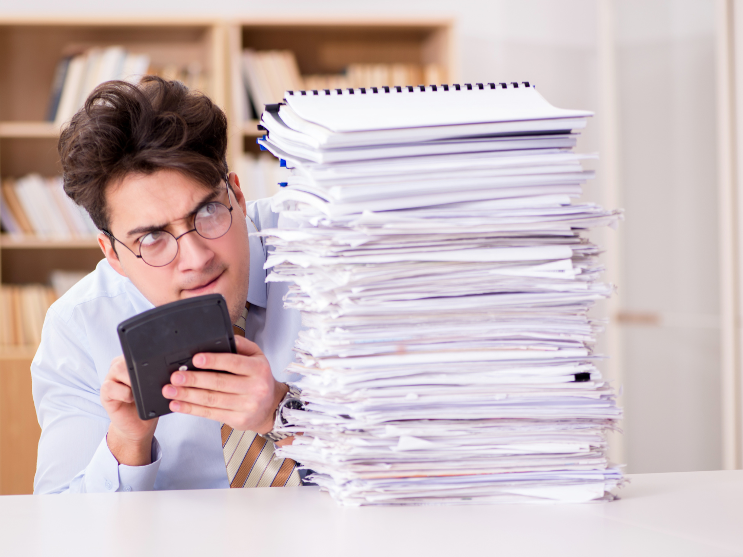 Business owner with a calculator peeking around a tall stack of unfiled paperwork